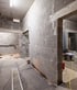 Indoor construction site featuring grey cinder block walls, concrete floors, and open doorways under bright work lights.