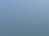 Eine schmutzige, cremefarbene Hauswand mit mehreren Fenstern und einem roten Dach unter blauem Himmel.