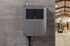 Graues elektronisches Steuergerät mit Display an einer Betonwand in einer Industriehalle.