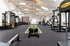 Moderner Fitnessraum mit Kraftstationen, Hantelbank, Schlitten auf Kunstrasenbahn und Technogym-Geräten in einer hellen Halle.