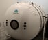 Man in a blue headrest inside a hyperbaric oxygen therapy chamber, looking upwards.