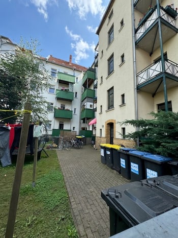 Blick durch den Innenhof zum Nachbargebäude mit Balkonen und Mülltonnen am Weg