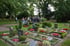 Menschengruppe geht auf einem Weg zwischen Grabsteinen und Blumenbeeten auf einem Friedhof.