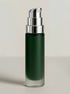 Dunkelgrüne, zylindrische Kosmetikflasche mit silbernem Spender auf hellgrauem Hintergrund.