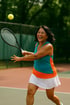 Eine lachende Frau mit Tennisschläger schlägt einen gelben Tennisball auf einem Tennisplatz.
