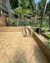 Geflieste Terrasse mit zwei Stufen, schmiedeeisernem Geländer und üppigem Grün im Hintergrund.