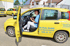 Eine lächelnde Pflegekraft sitzt in einem gelben Auto mit dem Logo "Pflegezentrum Eule GmbH", die Tür ist offen.