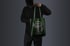 Person in schwarzer Kleidung hält eine grüne Stofftasche mit einem Comic-Roboter, der Brille und Kappe trägt.