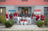 Ein Team von 16 Mitarbeitern in roten und grauen Uniformen steht vor dem Eingang der Zahnarztpraxis Dr. Michael Warwick.