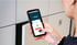 Person hält Smartphone mit Medigo-App, die eine Nummer 14 und einen orangenen Button anzeigt.