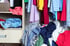 Unordentlicher Kleiderschrank mit bunten, zerknitterten Kleidungsstücken auf Böden und Kleiderstangen.