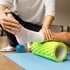 Physical therapist guides a patient's leg as they use a foam roller and massage ball.