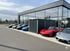 Mehrere Sportwagen parken vor einem modernen Autohaus mit Glasfassade, daneben ein Container in Anthrazit.