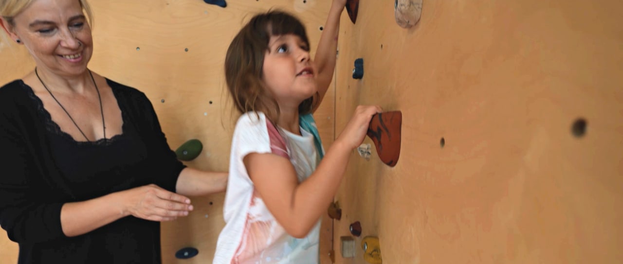 Therapeutin begleitet ein Mädchen an einer Kletterwand
