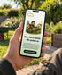 Smartphone zeigt die Website von Haus, Hof & Garten Service Stude mit einem Gärtner-Cartoon im sonnigen Garten.