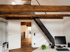 Modernes Home-Office mit rustikalen Holzbalken, schwarzer Metalltreppe, Schreibtisch und Blick in den Flur.