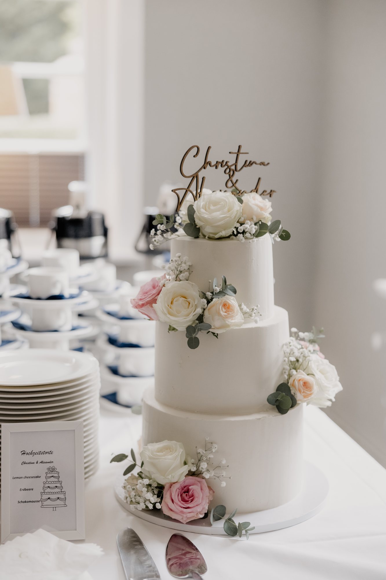 Dreistöckige Hochzeitstorte mit Rosen und Eukalyptus auf dem Buffettisch