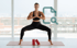 Frau macht Yoga-Übung auf Matte vor Fensterfront mit Stadtblick, daneben ein Lupen-Icon und rote Buchpakete am Boden.