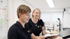 Zwei lächelnde Frauen in schwarzen Mission Kita Poloshirts arbeiten gemeinsam an einem Schreibtisch im Büro.