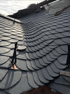 Dunkelgraues Schieferdach mit geschwungenen Schindeln, Kupferdetails und Dachhaken.