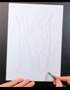 Eine Hand zeichnet wellenförmige vertikale Linien auf ein weißes Blatt Papier, um einen Baumstamm zu gestalten.