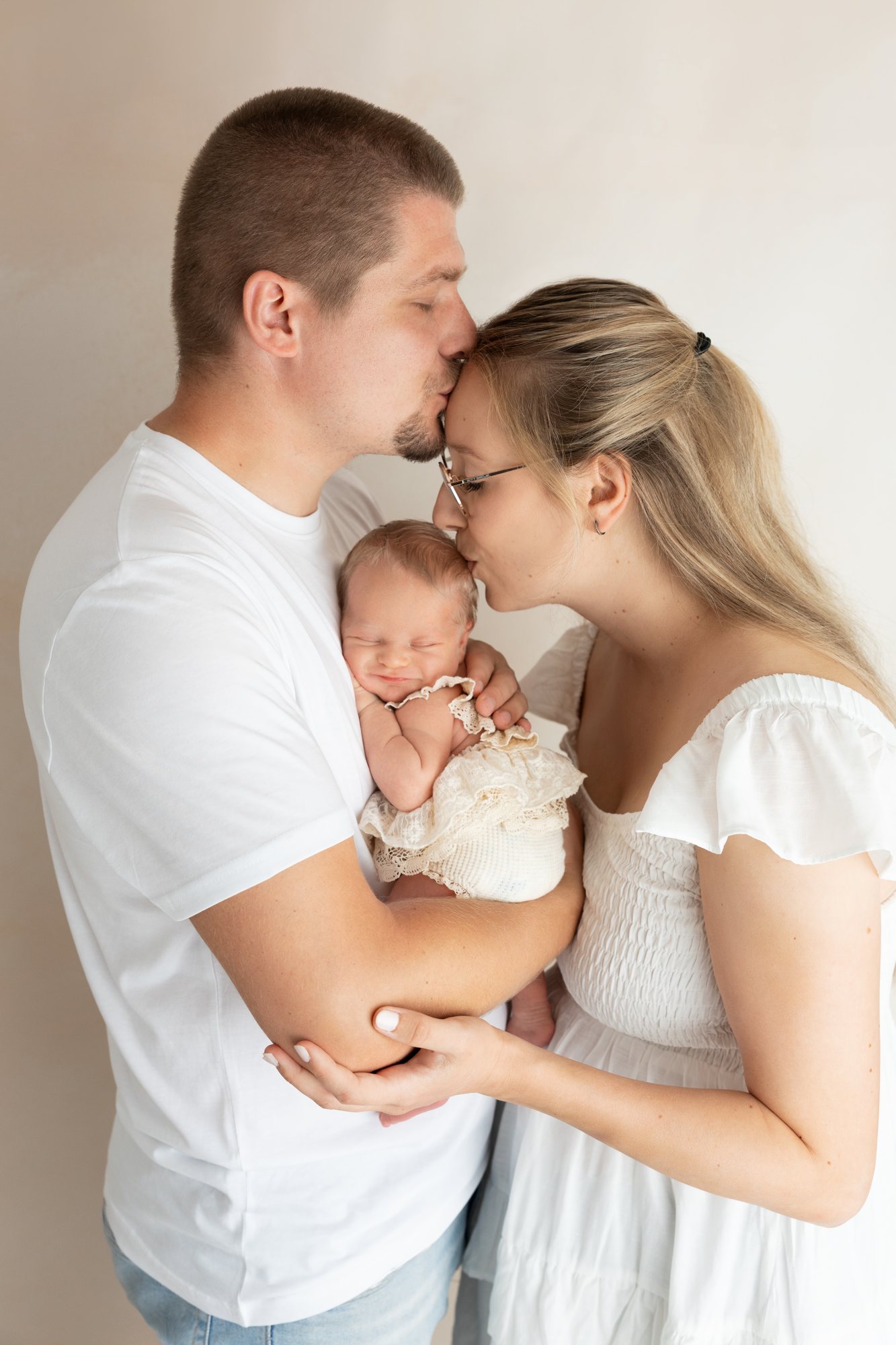 Vater küsst die Mutter auf die Stirn, während sie ihr Neugeborenes im Arm hält