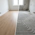 Vorher-Nachher-Vergleich: Ein Raum mit Holzboden und ein Raum mit Fußbodenheizungsschlangen im Rohbau.