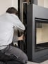 Ein Handwerker installiert oder wartet die interne Mechanik eines modernen, schwarzen Kamineinsatzes in einer Wand.