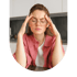 A woman with glasses rubs her temples with her eyes closed, appearing to have a headache or migraine.
