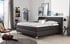 Ein Boxspringbett mit anthrazitfarbenem Stoffbezug steht in einem modernen Schlafzimmer.