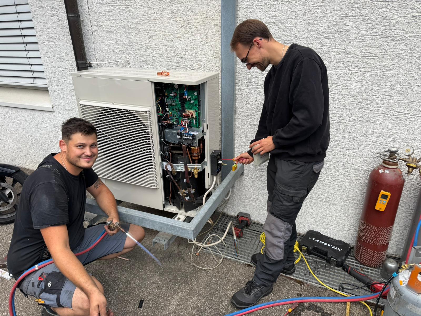 Zwei Monteure der AIR2S Klimatechnik schließen in Schönaich das Außengerät einer Klimaanlage an