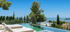Blick auf einen Infinity-Pool mit zwei Liegestühlen, dahinter das Meer und eine bewaldete Landschaft.
