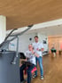 Zwei Männer zeigen den Daumen nach oben an einem Trainingsgerät in einem modern gestalteten Fitnessstudio mit Holzdecke.