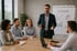 Ein lächelnder Mann präsentiert vor einer Flipchart mit "TRAINING" und Diagrammen an eine Gruppe von vier Kollegen.