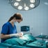 Chirurgin in blauer OP-Kleidung führt unter einer Operationsleuchte einen Eingriff an einem Patienten durch.