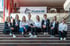 Acht Frauen sitzen auf einer Treppe vor einem FUCHS-Banner mit einem Wolfskopflogo und dem Text "SACHVERSTÄNDIGE & PRÜFINGENIEURE".