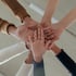 Mehrere Hände verschiedener Hautfarben liegen als Zeichen von Teamarbeit und Gemeinschaft übereinander.