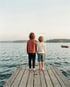 Zwei Kinder halten sich an der Hand und schauen von einem Steg über ruhiges Wasser
