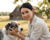 Eine Frau streichelt einen Australian Shepherd vor einer Scheune.