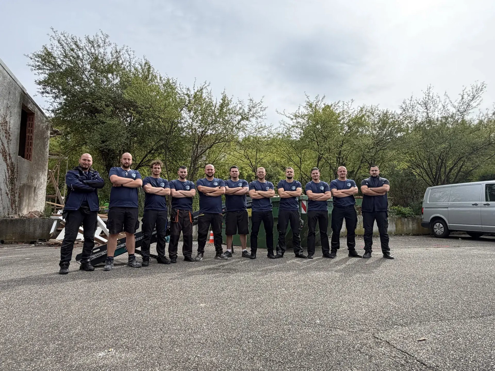 Das Team von Räum und Abrissprojekt: elf Mitarbeiter in Firmenshirts vor einem Container