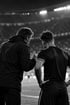 Trainer motiviert im Gespräch einen Spieler am Spielfeldrand eines Spielfelds in einer ausverkauften Arena
