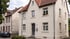 Zweistöckiges, hellbeiges Wohnhaus mit Satteldach, roten Ziegeln und blauer Eingangstür unter bewölktem Himmel.