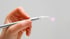 Hand hält einen silbernen Dental-Laserstift mit einer weißen Spitze, aus der ein violetter Lichtpunkt strahlt.