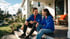 A man and a girl in blue sweatshirts sit on the front porch steps of a white suburban house, smiling at each other.