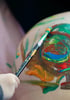 Bunter Pinsel malt kreative Formen auf den Babybauch – Bodypainting während der Schwangerschaft, fotografisch festgehalten.