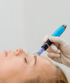 Eine Person erhält eine Microneedling-Behandlung an der Stirn, durchgeführt von einer Person mit Handschuh.