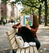 Frau sitzt auf Parkbank, liest Zeitschrift "THE CREATIVE REVIEW", Gesicht ist verdeckt.