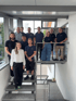 Das Team von Grickscheit steht lächelnd auf einer Treppe und Plattform in einem modernen Gebäude.