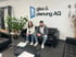 Zwei Personen sitzen auf schwarzem Ledersofa unter dem Logo "glas & planung AG" an einer weißen Wand.