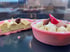 Eine ganze und eine halbierte rosa Torte mit Mandeln und Puderzucker auf schwarzem Hintergrund.